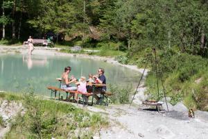 un grupo de personas sentadas en una mesa de picnic junto a un lago en Das kleine Paradies en Unken