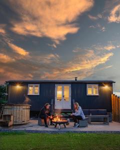 deux personnes assises autour d'un foyer extérieur devant une petite maison dans l'établissement Inglewood Shepherd's Huts, à Penrith
