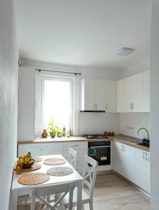 cocina con armarios blancos, mesa y sillas en Solomon Apartments ap 2 en Sîngeorgiu de Mureş