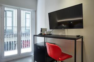 a red chair sitting in front of a desk with a television at Ella Hostel Ramblas in Barcelona