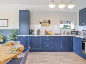 a kitchen with blue cabinets and a wooden table at Whileaway Cottage in Looe