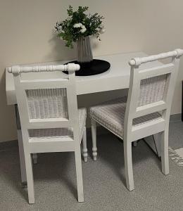 una mesa blanca con 2 sillas y un jarrón con flores en Butas Senamiestyje en Rokiškis