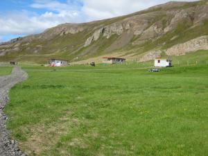 a field of green grass with houses and a mountain at Ásbrandsstadir Cottage in Vopnafjörður