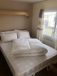 a large white bed in a bedroom with a window at A4 THE CHASE 6 Berth Pet Friendly Caravan With Decking in Ingoldmells
