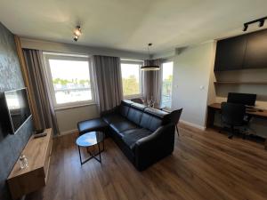 a living room with a black leather couch and a desk at Tricity Apartments - Wilga Park in Gdańsk