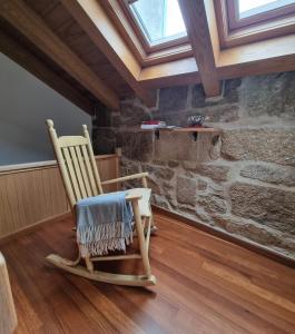 uma cadeira de balanço de madeira num quarto com uma parede de pedra em Casa mariñeira San Tomé em Cambados