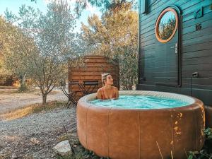 a man sitting in a hot tub in a backyard at Roulottes et Cabanes de Saint Cerice in Vogüé