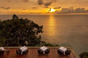 a sunset over the water with umbrellas on a deck at Paresa Resort Phuket - SHA Extra Plus in Kamala Beach