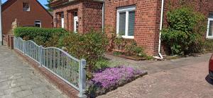 une clôture devant un bâtiment en briques avec des fleurs violettes dans l'établissement Ferienwohnung am Vareler Hafen/ Nordsee, à Varel