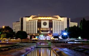 a large building with a pond in front of it at night at Marina Apartment in Sofia