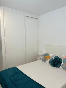 Un dormitorio blanco con una cama con almohadas azules. en 2 Jj e Hijos Conil SL, en Conil de la Frontera