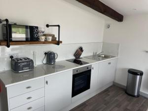a kitchen with white cabinets and a sink and a microwave at The Old Piggery Barn in Longton