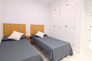 2 camas en una habitación con paredes blancas en El Patio del Sol, apartamentos Living Sur, en Sanlúcar de Barrameda