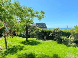 une cour verdoyante avec des arbres et une maison en arrière-plan dans l'établissement Superbe villa vue sur mer, corniche de la plage, à Bénodet