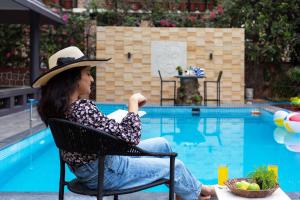 een vrouw in een stoel naast een zwembad bij Sunshine Bloom by StayVista - Your Oasis with Pool, Lawn, Gazebo, and Poker Table in Lonavala
