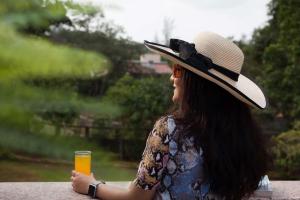 een vrouw met een hoed en een glas sinaasappelsap bij Sunshine Bloom by StayVista - Your Oasis with Pool, Lawn, Gazebo, and Poker Table in Lonavala