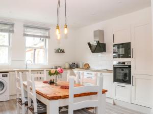 uma cozinha branca com uma mesa de madeira e cadeiras em The Apothecary em Brockenhurst