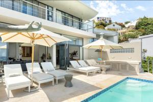 een zwembad met stoelen en parasols naast een gebouw bij CapeStays - Villa Infinity in Kaapstad