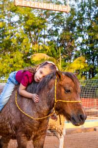 a little girl laying on the back of a pony at Pousada Vale dos Tamanduás in Olímpia