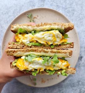 a person holding up a sandwich with eggs and lettuce at Hostel 35 in Al Madinah