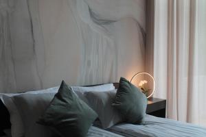 Cama con almohadas grises y mesa con lámpara en Green Valley Loft, en Jūrmala