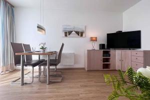 uma sala de estar com uma mesa com cadeiras e uma televisão em Ferienwohnung-47-mit-Schwimmbad-Sauna-Residenz-Passat-Doese em Cuxhaven