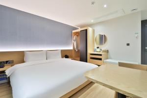 Un dormitorio con una gran cama blanca y una mesa en Custom Hotel en Ulsan