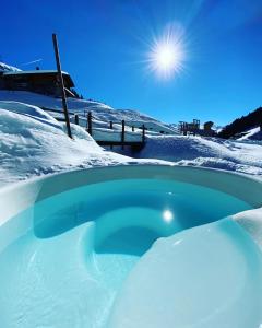 uma banheira de hidromassagem coberta de neve com o sol ao fundo em Berglodge Ascharina em Sankt Antönien