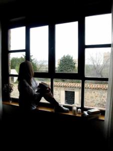 a woman sitting on a window sill reading a book at Casa del Puente Muralla Homes in Avila