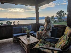 une femme assise sur une terrasse couverte donnant sur l'eau dans l'établissement Rustic House Radovic, à Knić