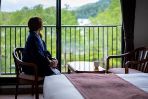 Kobieta siedząca na krześle patrząca przez okno w obiekcie KAMENOI HOTEL Okunikko w mieście Nikko