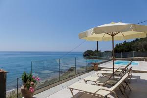 eine Terrasse mit Stühlen, einem Sonnenschirm und dem Meer in der Unterkunft Villa Renata & Villa Filippos with private Plunge Pool by Konnect in Agios Gordios