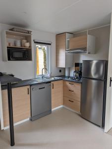 cocina con armarios de madera y nevera de acero inoxidable en Mobil Home LUXE de 44m2 Les pieds dans l'eau Ménage et draps inclus Camping 5 Etoiles Lac Biscarrosse Koyobalys, en Biscarrosse