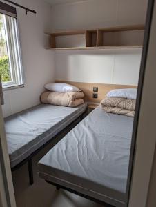 Habitación pequeña con 2 camas y ventana en Mobil Home LUXE de 44m2 Les pieds dans l'eau Ménage et draps inclus Camping 5 Etoiles Lac Biscarrosse Koyobalys, en Biscarrosse