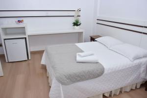 a white bedroom with a bed and a desk at Avenida Hotel in São Lourenço do Oeste