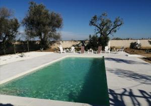 uma piscina com cadeiras brancas e um pátio em Casa Serradei em Torchiarolo