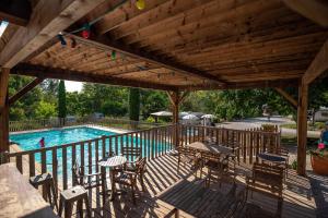 a wooden deck with tables and chairs and a swimming pool at Camping Beau Rivage in Navarrenx