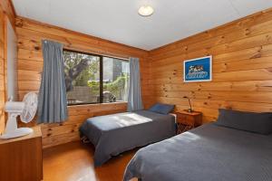Duas camas num quarto com paredes de madeira e uma janela em Karaka Bach - Mangawhai Heads Holiday Home em Mangawhai