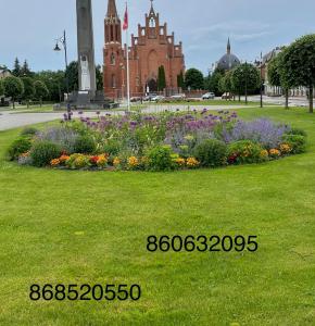 um círculo de flores num parque com uma igreja em Butas Senamiestyje em Rokiškis