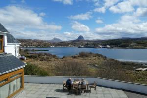 a man sitting at a table on a patio overlooking a lake at Caisteal Liath House in Lochinver