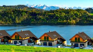 a row of houses on a lake with mountains in the background at Czorsztyn Prestige Apartamenty in Czorsztyn +111 photos