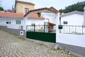 a white house with a green gate on a street at Casinha da Eira in Góis