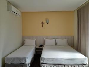 2 Betten in einem Zimmer mit einem Kreuz an der Wand in der Unterkunft CEIC Pousada e Eventos in Nova Trento