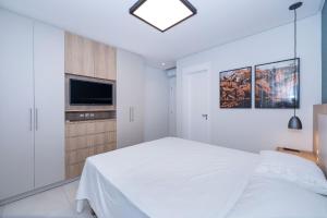 ein weißes Schlafzimmer mit einem Bett und einem Fernseher in der Unterkunft Adra 301 - Apartamento no centro de Bombinhas - Rooftop com piscina e academia - À poucos metros da praia - (Consultar serviços de roupas de cama e banho) in Bombinhas + 30 Fotos