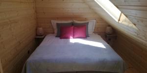 a bed with two pink pillows in a wooden room at Woodorf drewnem usłane - domki z bala nad rzeką Słupią wśród pól i lasów z chatą grillową, ogniskiem i placami zabaw dla dzieci -Royal Red House z jacuzzi i ogrodzonym extra ogródkiem dla piesków, Royal Green House - bez jacuzzi in Ustka