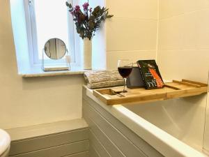 a glass of wine and a book on a shelf in a bathroom at Key Cottage, sleeps 8 in Brimscombe