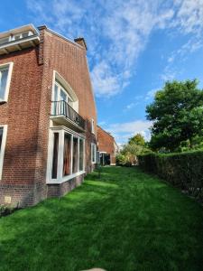 une maison en briques avec une cour d'herbe devant elle dans l'établissement Cozy Garden House kijkduin Beach, à La Haye
