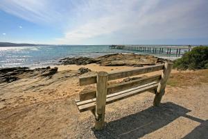 una panchina di legno seduta su una spiaggia con un molo di Beachside At Breakers a Lorne