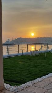 a sunset over the water with a bench in the grass at BEDWAVE Seaside Mansion in Piraeus