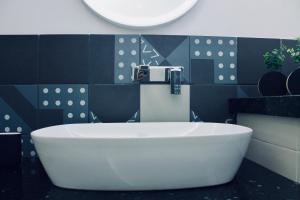 a large white tub in a bathroom with black tiles at Di Rosa Apartment in Avola +22 photos